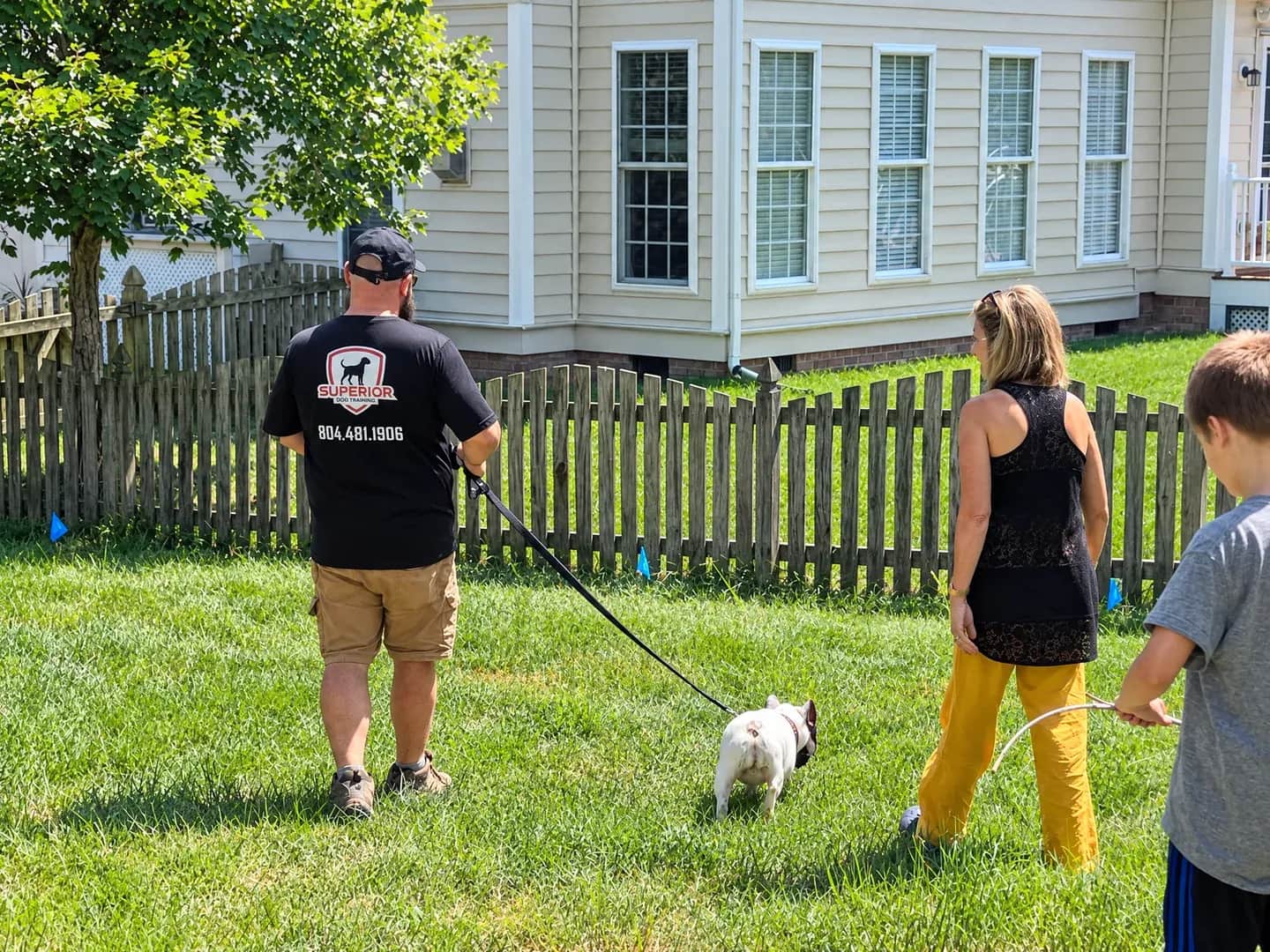 People practicing with a dog on a leash in a yard.